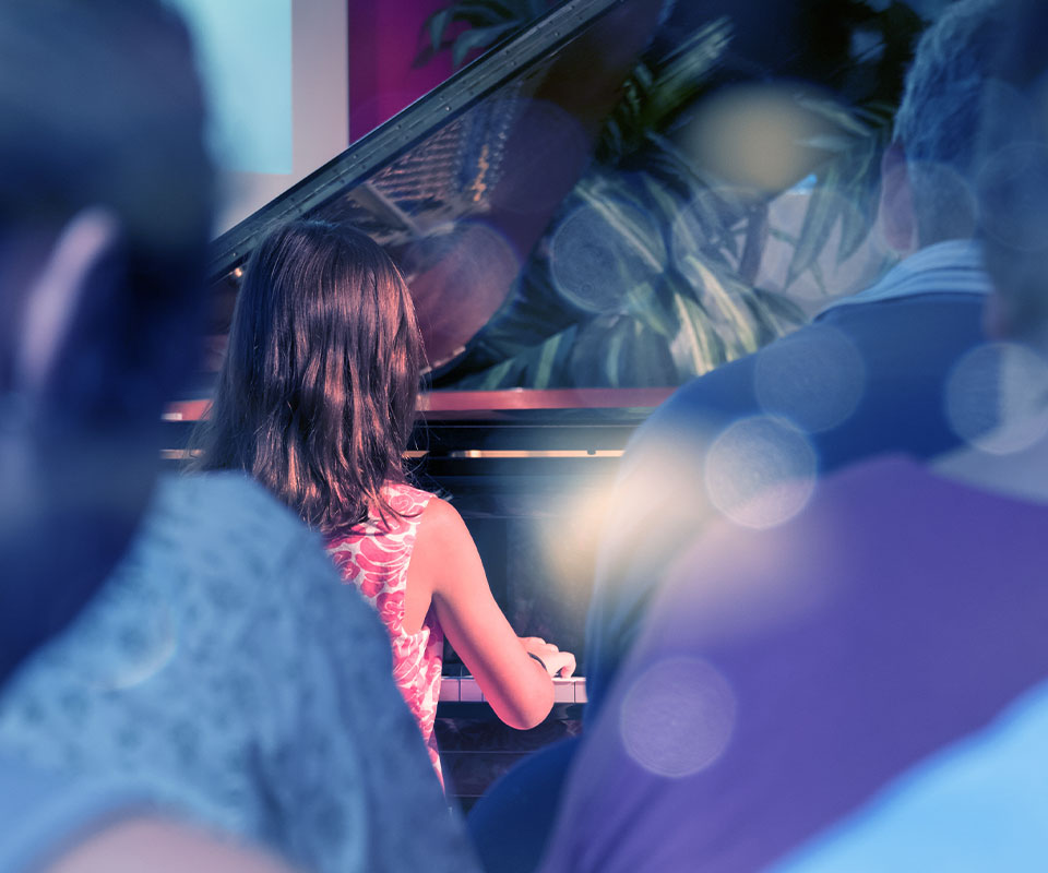 image of girl playing at piano recital in front of people